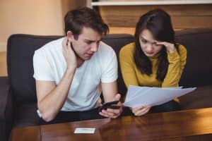 Casal preocupado sentado no sofá olhando para contas e um celular, simbolizando estresse financeiro e dificuldade em pagar dívidas.