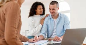 Casal sorridente analisando documentos financeiros em casa, representando planejamento financeiro e organização de contas.