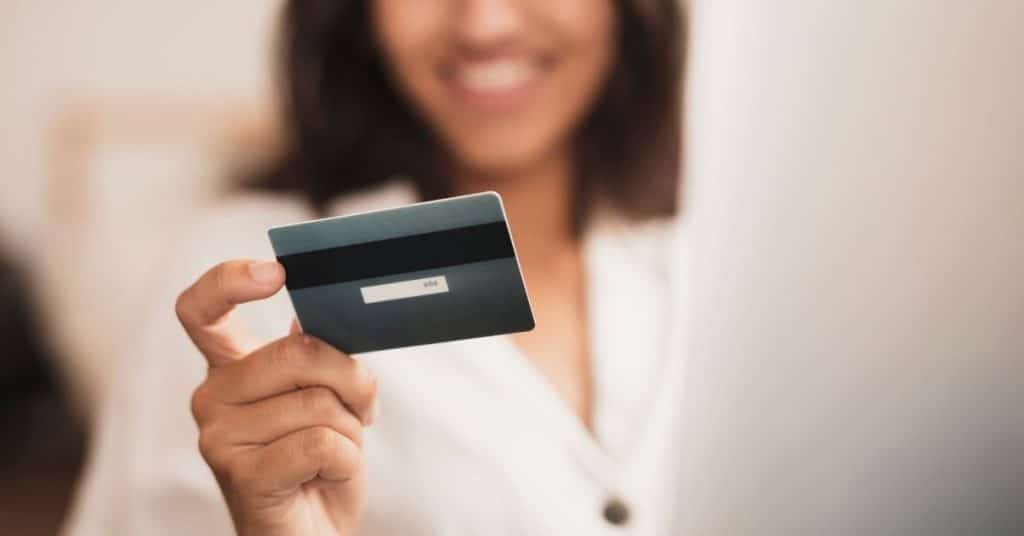 Mulher sorridente segurando um cartão de crédito, representando o uso moderno de cartões para acumular milhas e benefícios financeiros.