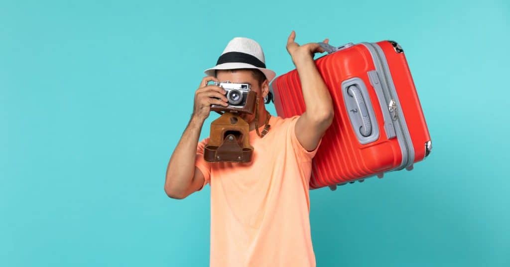 Viajante segurando uma mala vermelha e tirando foto com uma câmera, representando viagens internacionais e turismo.