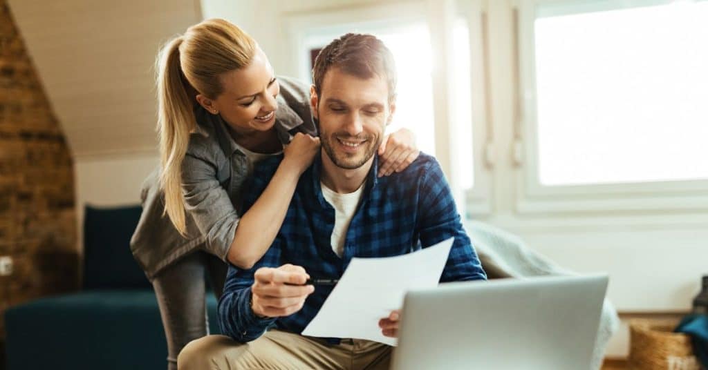 Casal jovem assinando contrato com corretor, simbolizando planejamento financeiro e decisões sobre investimentos ou crédito.