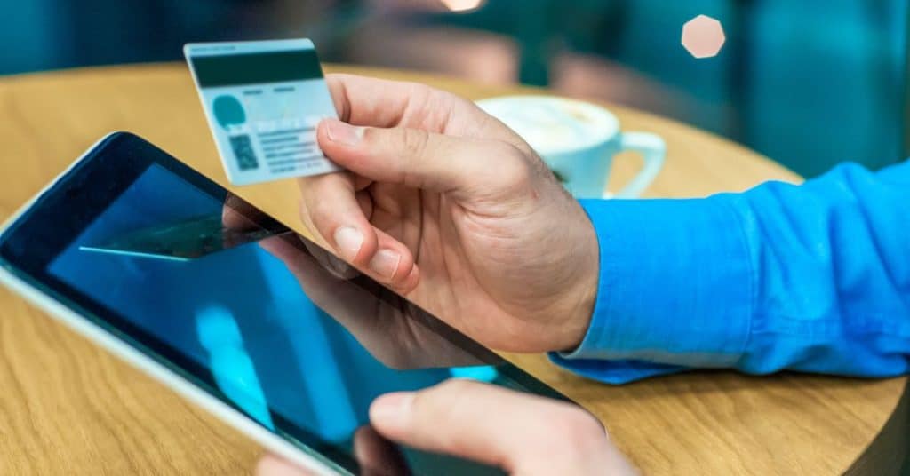 Pessoa segurando um cartão de crédito enquanto faz compra online em um tablet, representando pagamentos digitais e segurança financeira.